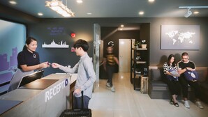 A reception area with a counter labeled "RECEPTION," a world map on the wall, and a seating area with guests. - Kokotel Bangkok Sukhumvit 50 (Bangkok)