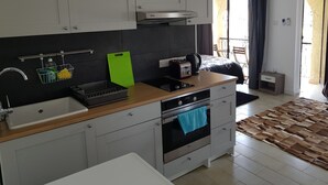 A compact kitchen with a sink, stove, and a small countertop. There is a window with curtains, a wooden floor, and a rug. - Mylos Court Apartments (Limassol)