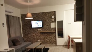 A modern living room with a stone wall, a flat-screen TV, a sofa, a coffee table, and a dining area. - Mylos Court Apartments (Limassol)