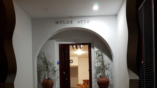 A staircase leading to a door with the sign "MYLOS APTS" above it. There are two large potted plants on either side of the door. - Mylos Court Apartments (Limassol)