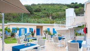 An outdoor patio area with white tables and chairs, blue tablecloths, and a staircase leading to an upper level. - Galìa Luxury Resort (Pizzo)