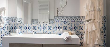 Un baño con un lavamanos blanco, azulejos con diseño azul, un espejo y un perchero con toallas.