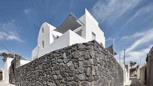 A modern white building with a stone wall in front. - Alchemy Luxury Villa (Santorini)