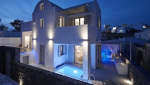 A modern two-story house with a swimming pool, outdoor seating, and a well-lit patio area. - Alchemy Luxury Villa (Santorini)