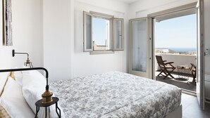A bedroom with a bed, a nightstand, a window, and a balcony with a view. - Alchemy Luxury Villa (Santorini)