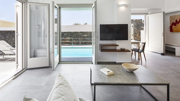 A modern living room with a sofa, a coffee table, and a TV mounted on the wall. - Alchemy Luxury Villa (Santorini)