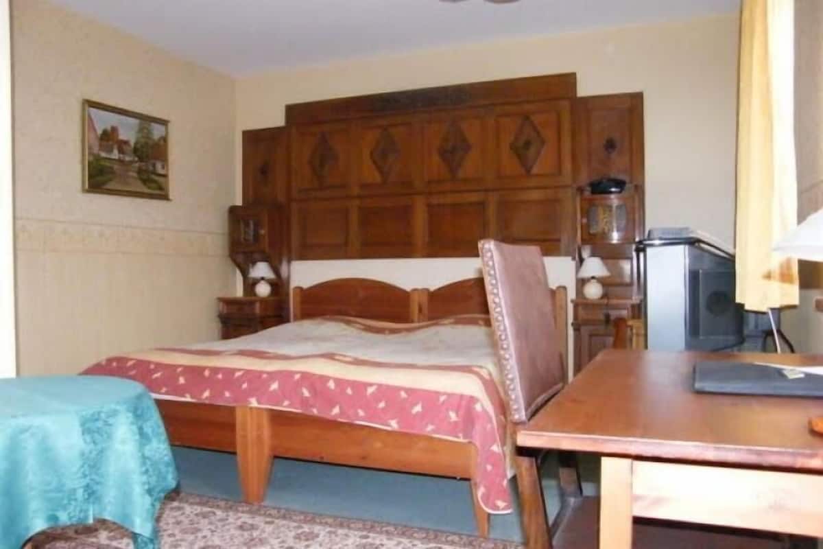 Un dormitorio con cama de madera, escritorio y silla. Hay un cuadro en la pared y una lámpara en el escritorio.