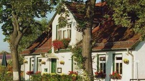 Ein zweistöckiges Gebäude mit weißer Fassade, grünen Fensterläden und zahlreichen Fenstern.