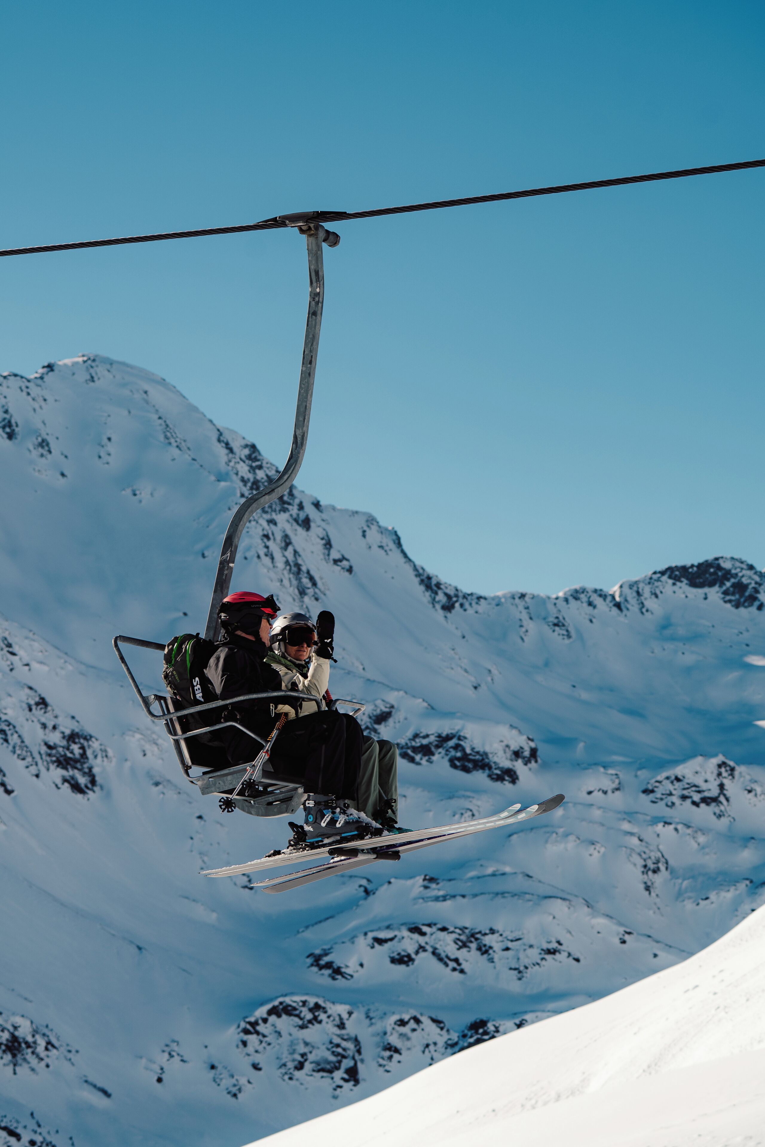 Een skiflift met twee skiërs in een stoel, omgeven door besneeuwde bergen.