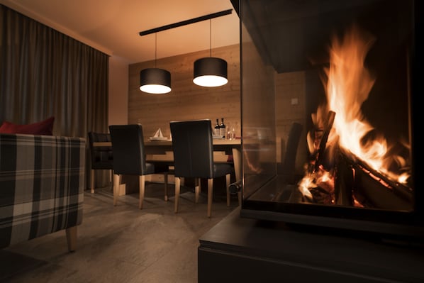 A modern living room with a fireplace, a dining area with wooden furniture, and a cozy seating area with a plaid sofa. - Arlberg Resort Klösterle (Klösterle am Arlberg)