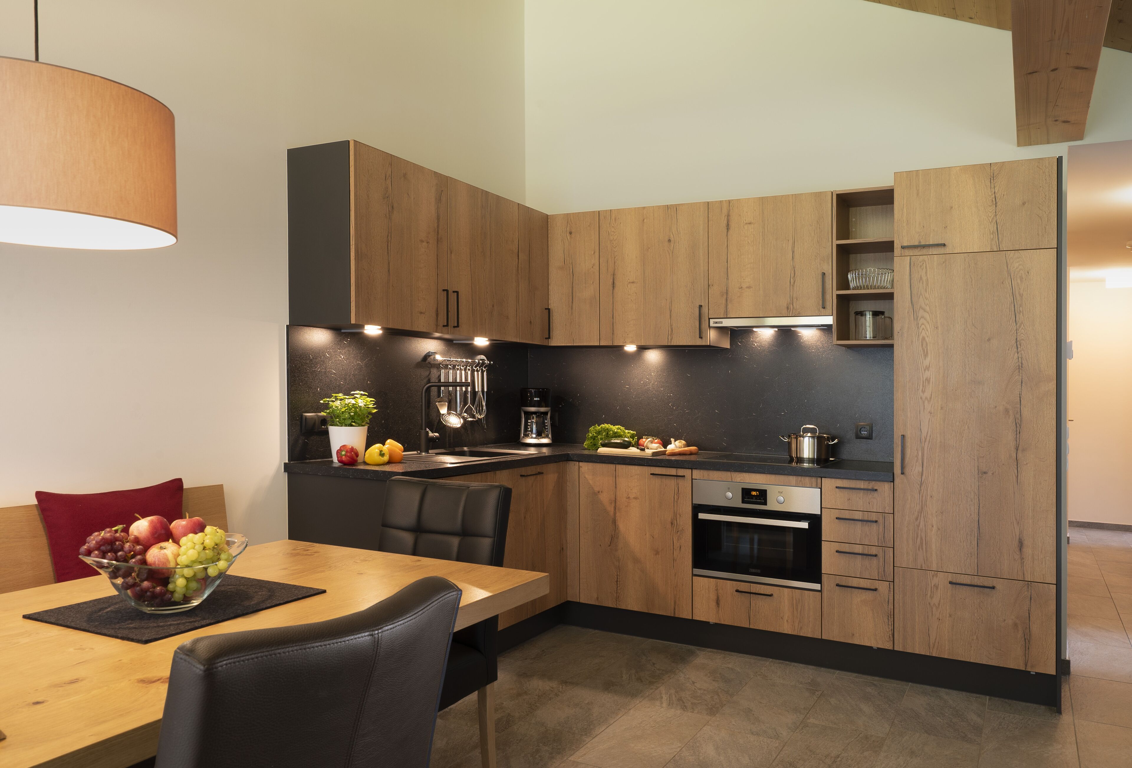A modern kitchen with wooden cabinets, a built-in oven, and a dining area with a table and chairs.