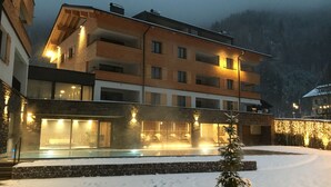 A multi-story building with a glass facade, a snow-covered ground, and a small tree in the foreground. - Arlberg Resort Klösterle (Klösterle am Arlberg)