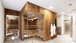 A modern spa area with wooden paneling, a glass-enclosed sauna, and a bench. - Arlberg Resort Klösterle (Klösterle am Arlberg)