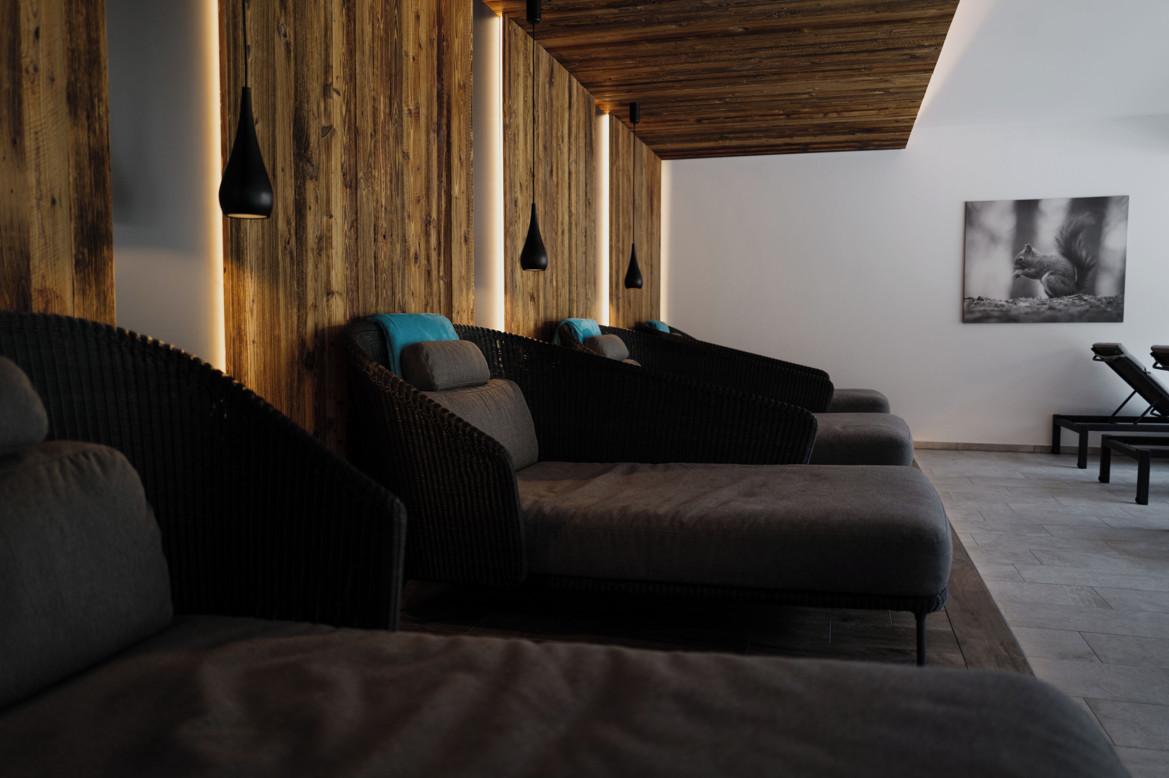 Una habitación con pared de madera, una lámpara colgante negra, un sofá con cojines y un cuadro enmarcado en la pared.