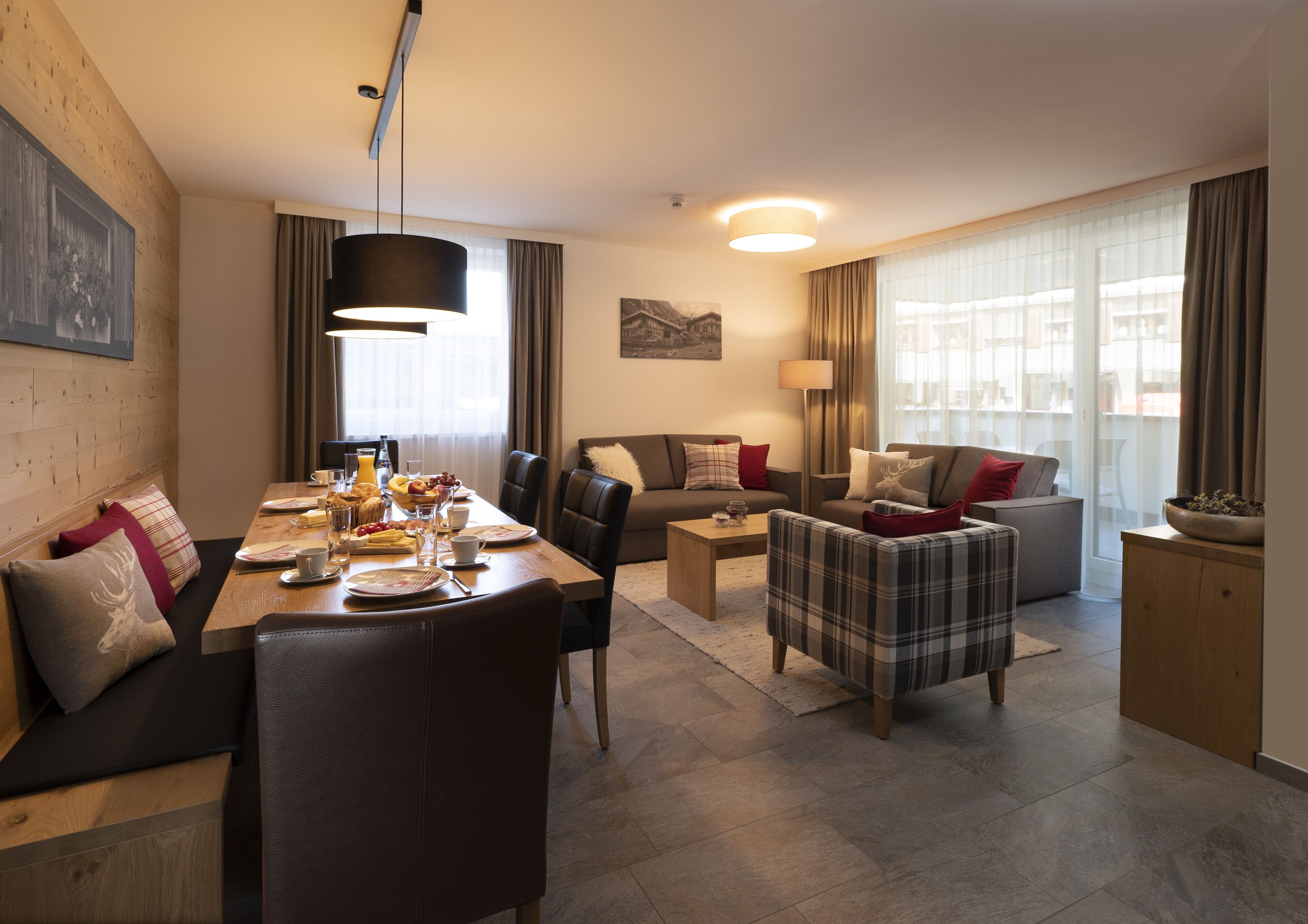 Una habitación de hotel moderna con zona de comedor, sofá, mesa de centro y vista a la ciudad.