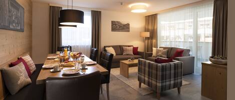 Una habitación de hotel moderna con zona de comedor, sofá, mesa de centro y vista a la ciudad.