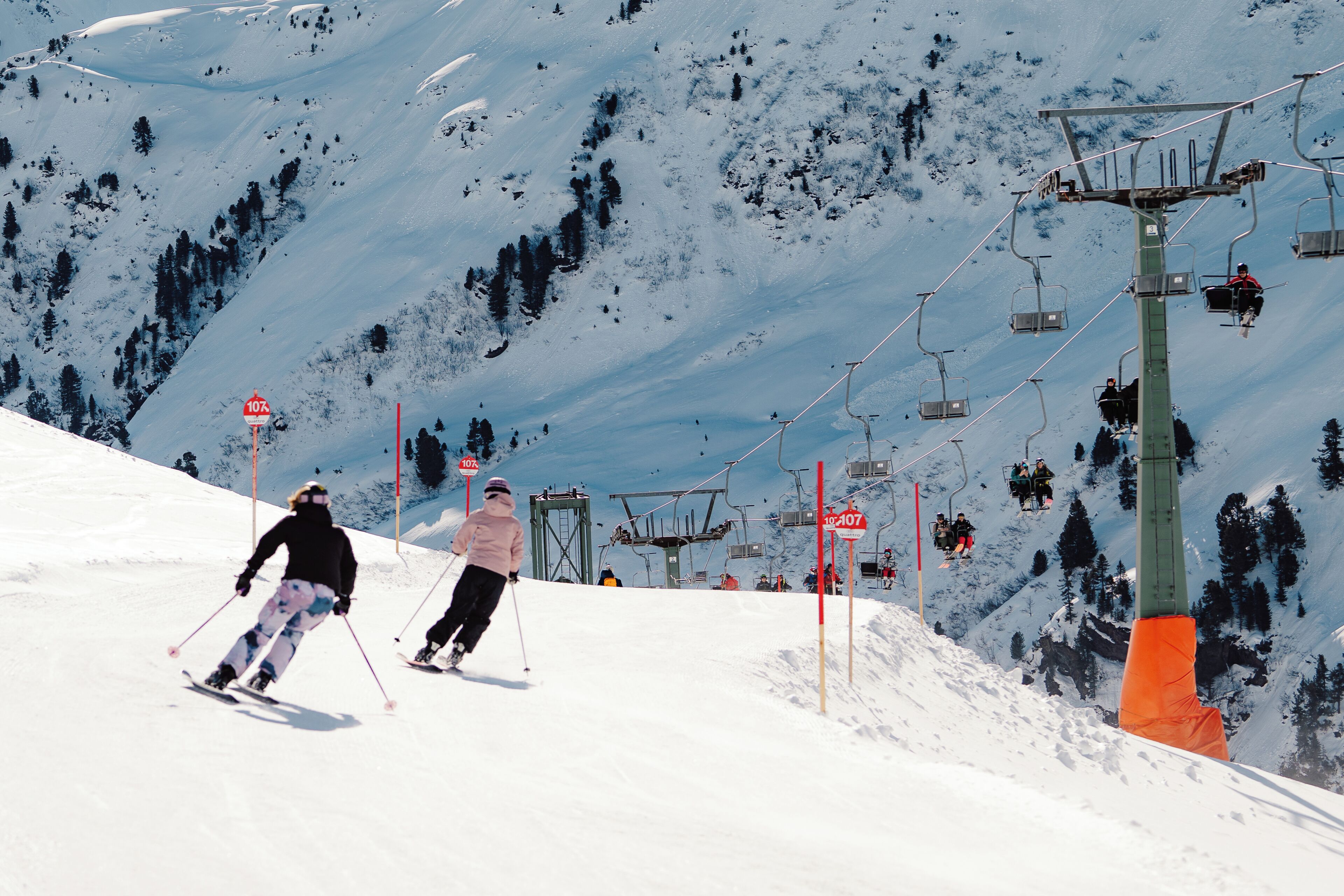 Eine Skipiste mit Skifahrern, einer Seilbahn und einem Berg im Hintergrund.