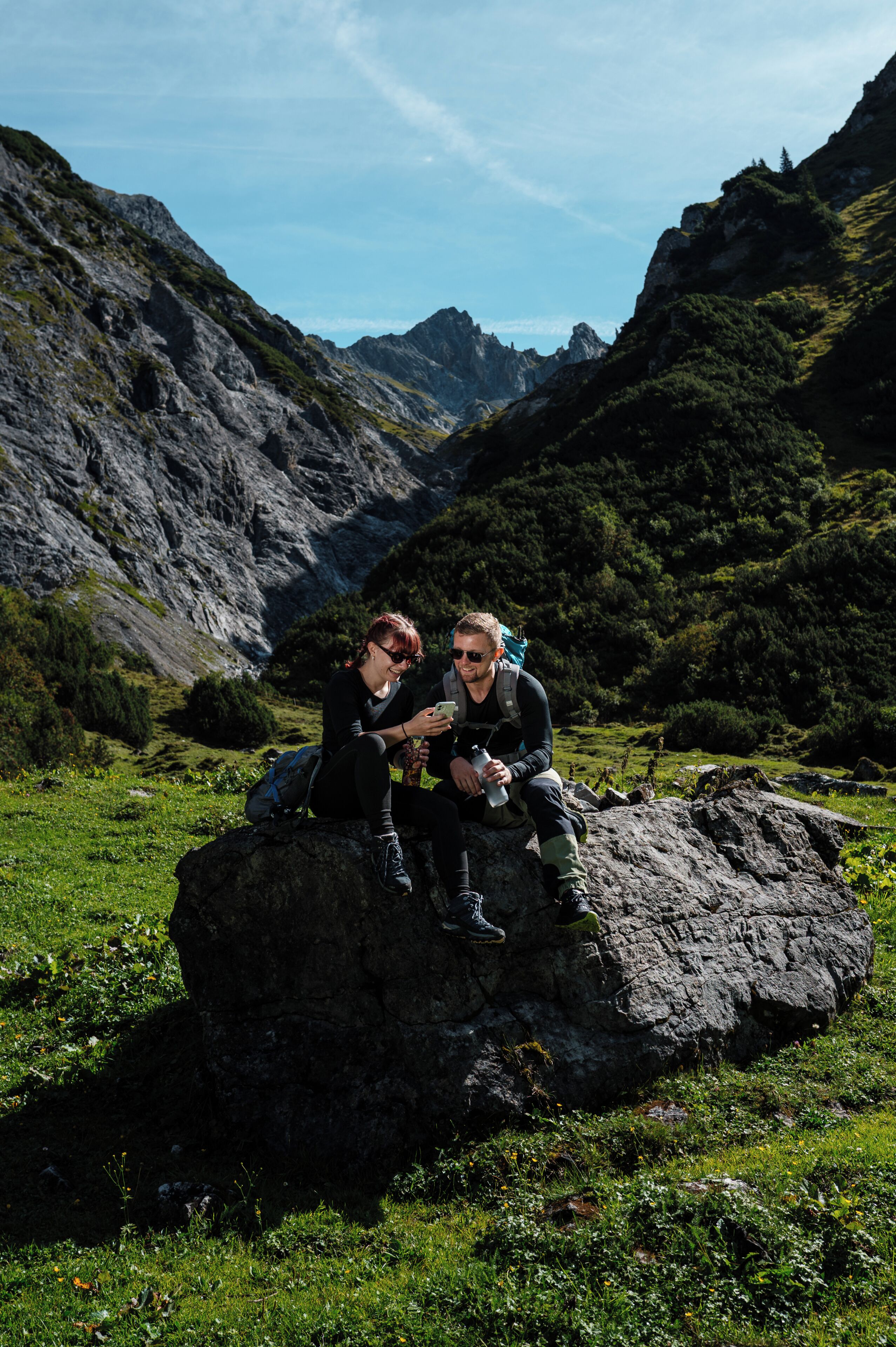 Two people sitting on a rock in a mountainous area.