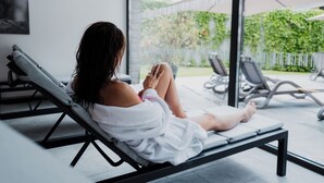 A person relaxing on a sun lounger in a modern indoor pool area with a view of a garden. - Arlberg Resort Klösterle (Klösterle am Arlberg)