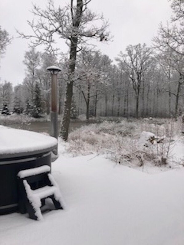 Een sneeuveld bedekte jacuzzi, omgeven door een besneeerd landschap met bomen.
