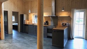 A spacious kitchen with wooden walls and a large island, equipped with modern appliances and ample counter space. - Stylish Lake house, outdoor hottub Lake view Close to nature. Pet friendly. (Våxtorp)