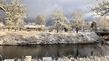 Een winterlandschap met een bevroren rivier, kale bomen en een brug op de achtergrond.