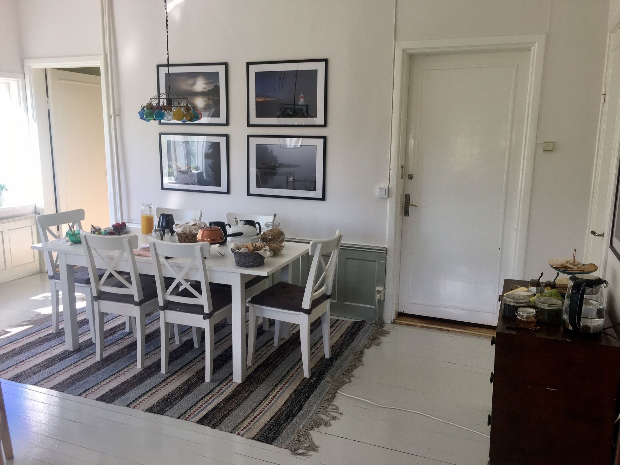 Un comedor con una mesa y sillas blancas, cuadros en la pared y un tapete a rayas.