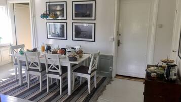 Un comedor con una mesa y sillas blancas, cuadros en la pared y un tapete a rayas.
