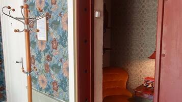 A room with a floral wallpaper, a wooden coat rack, and a red door leading to another room.