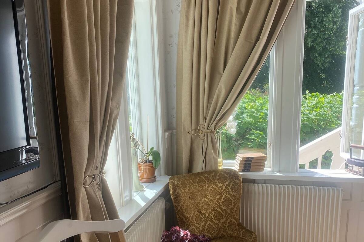 A cozy room with a patterned armchair, a small table with a vase of flowers, and a radiator.