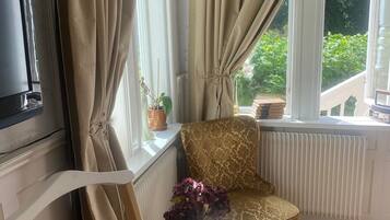 Um quarto acolhedor com uma poltrona estampada, uma mesinha com um vaso de flores e um radiador.