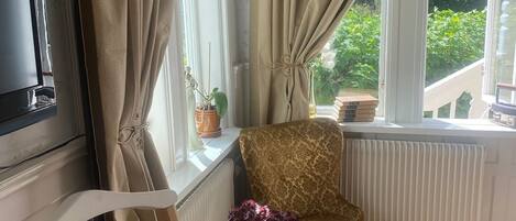 A cozy room with a patterned armchair, a small table with a vase of flowers, and a radiator.