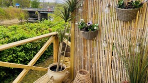 Um deck de madeira com cerca de bambu, uma planta em vaso e uma cesta de vime com flores.