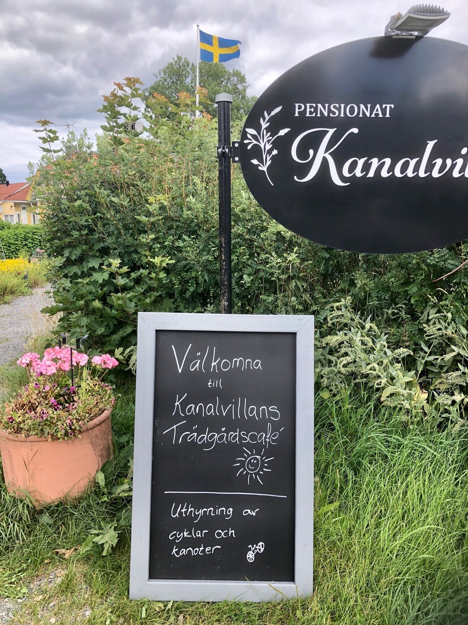 A signboard with the text "Välkommen till Kanalvillans Trädgårdscafe" and a chalkboard below it with "Uthyrning av cyklar och kanoter" written on it.