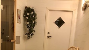 Quarto de canto com cadeiras de vime, uma pequena mesa, uma porta branca e área de chuveiro com box de vidro.