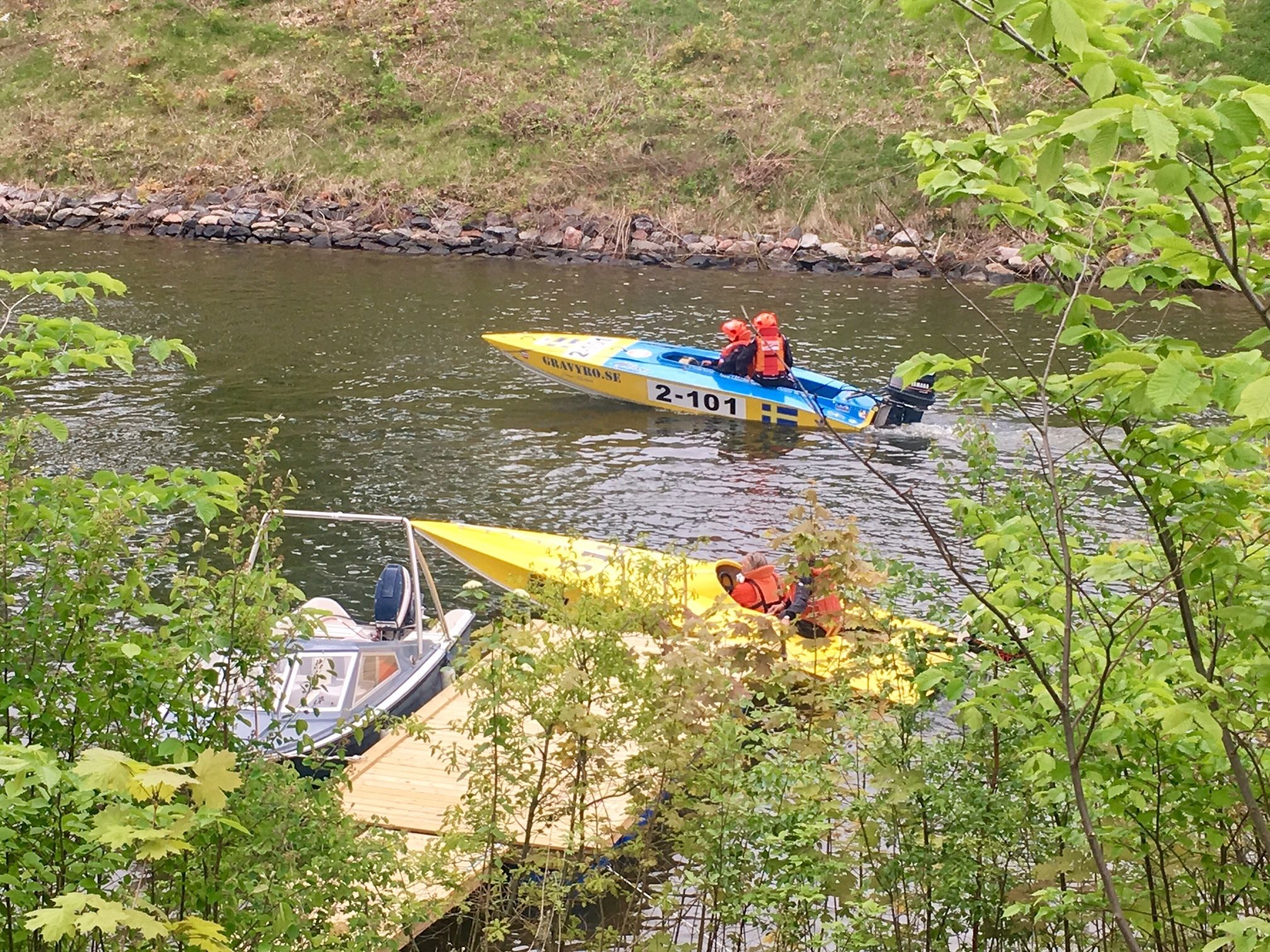 Twee boten op een rivier, één met een blauw-geel kleurenschema en de andere geel, beide met mensen die een reddingsvest dragen.