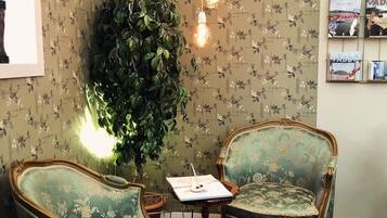 A room with floral wallpaper, two vintage-style chairs, a small table, and a large green plant.