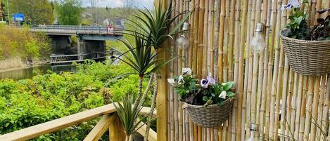 A wooden deck with a bamboo fence, potted plants, and outdoor furniture.