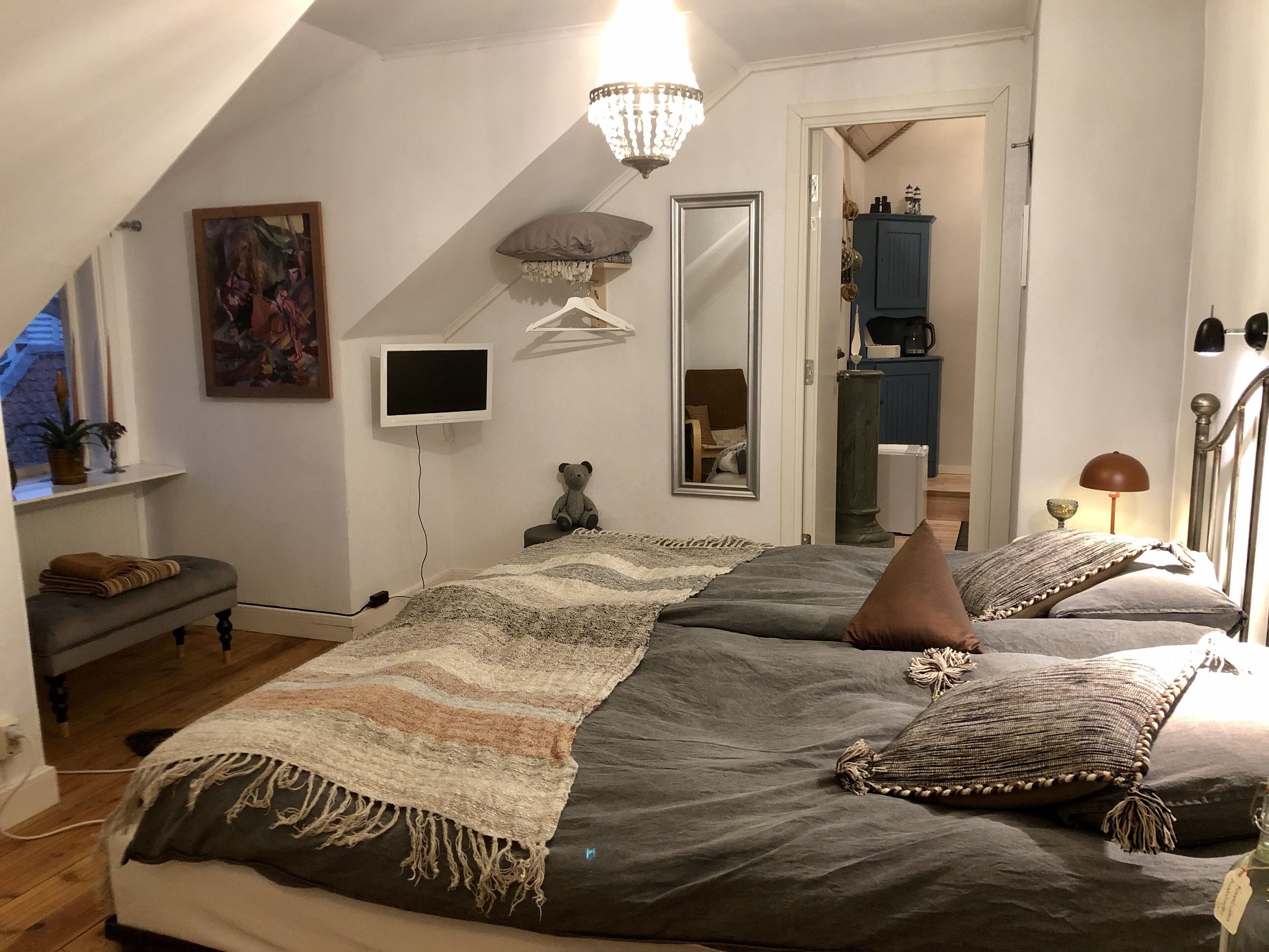 Ein Schlafzimmer mit einem großen Bett, einem Fernseher, einem Spiegel und einer Kristallleuchtre.'