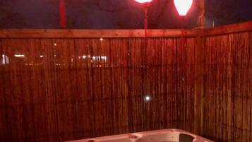 Een hottub in een omheind buitengebied met verlichting.