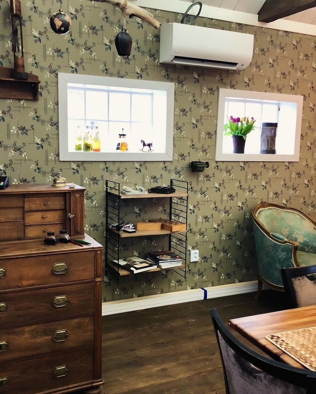 A room with floral wallpaper, a wooden dresser, a metal shelf unit, and a vintage chair.