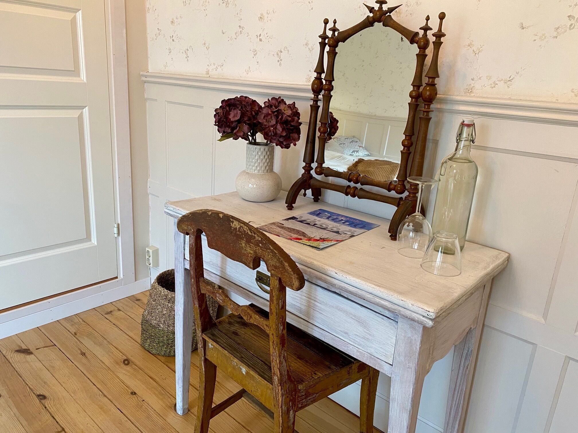 En sminkbord i vintage-stil med en spegel, en vas med blommor och en flaska.