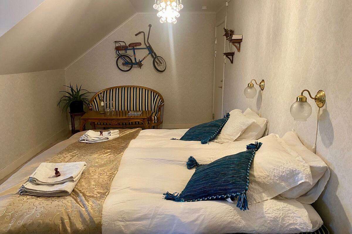 A bedroom with a bed, a chair, a table, a bicycle, and wall-mounted lamps.