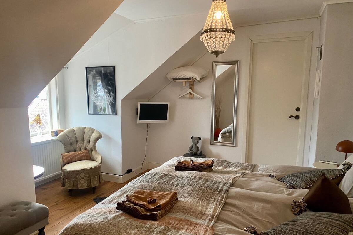A bedroom with a large bed, a chair, a television, a mirror, and a chandelier.