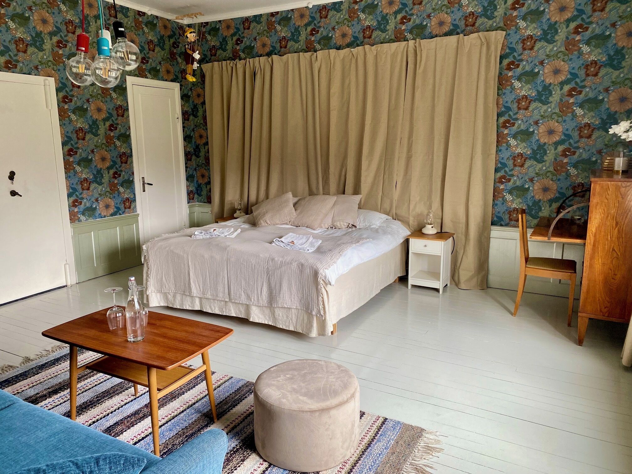 Een slaapkamer met een bed, nachtkastje, stoel en een bijzettafeltje met glazen.