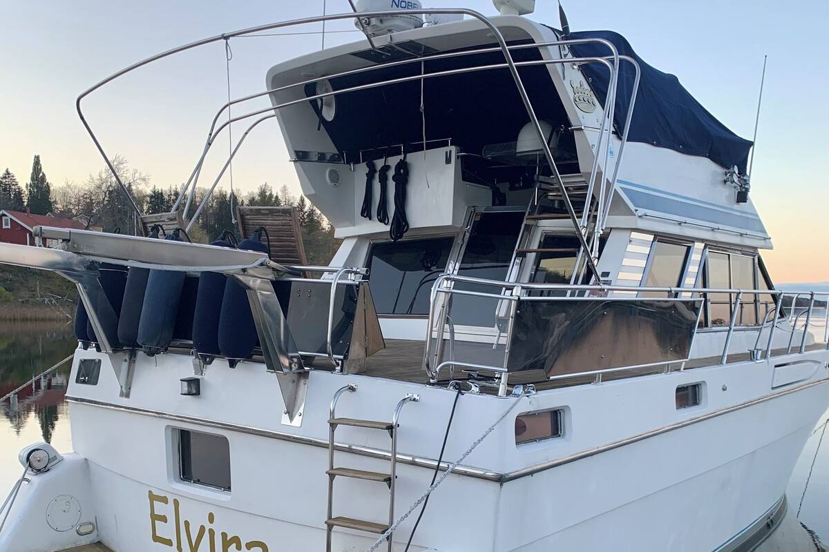 A white yacht named 'Elvira' docked at a marina with a covered deck area, a small cabin, and a wakeboard.