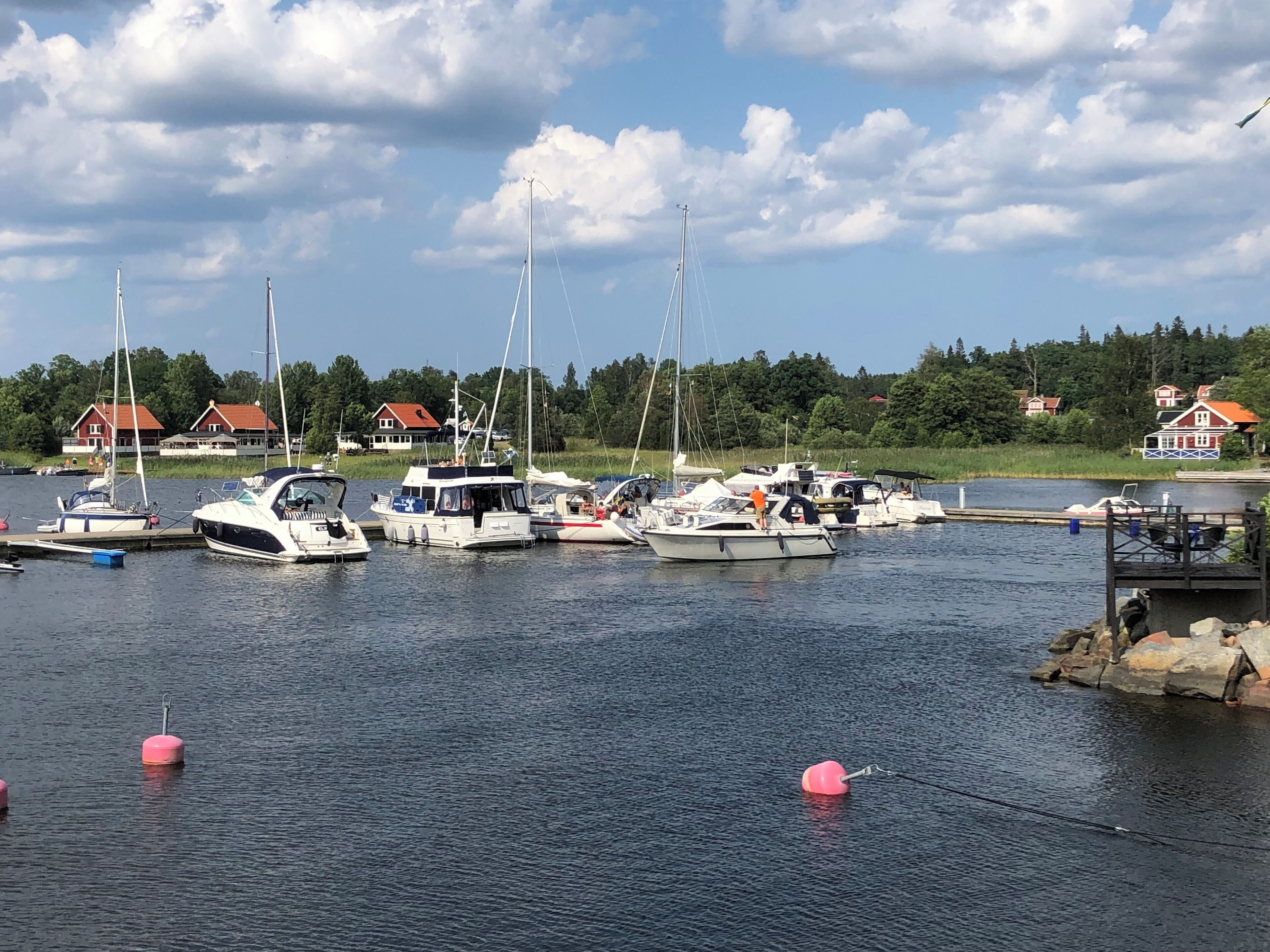 A marina with several boats docked, a dock with a small structure, and houses in the background.