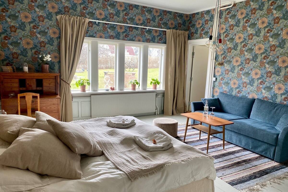 A cozy room with a bed, a blue sofa, a small table, and a window with curtains.