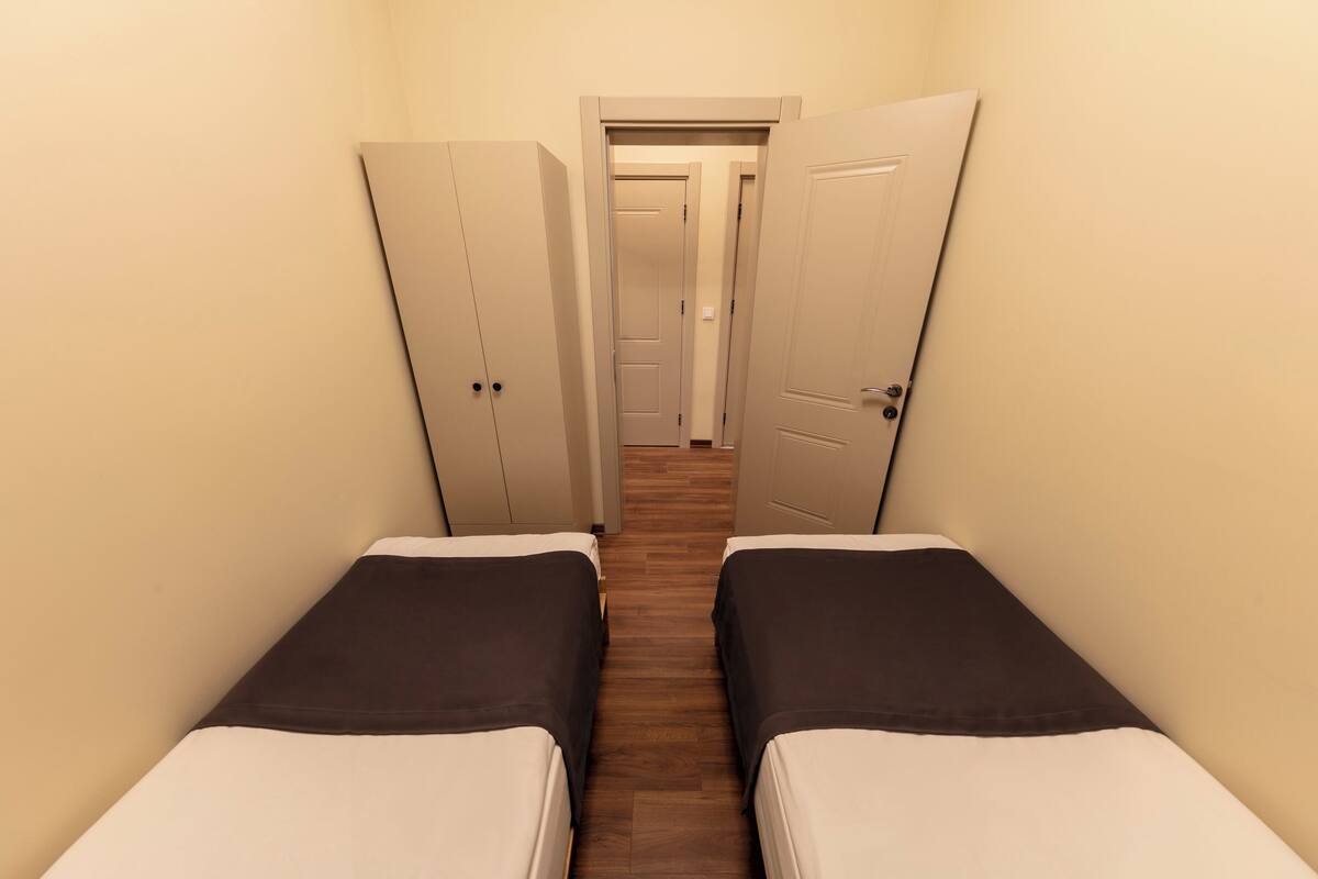 A narrow hallway with two beds on either side, leading to a door at the end.