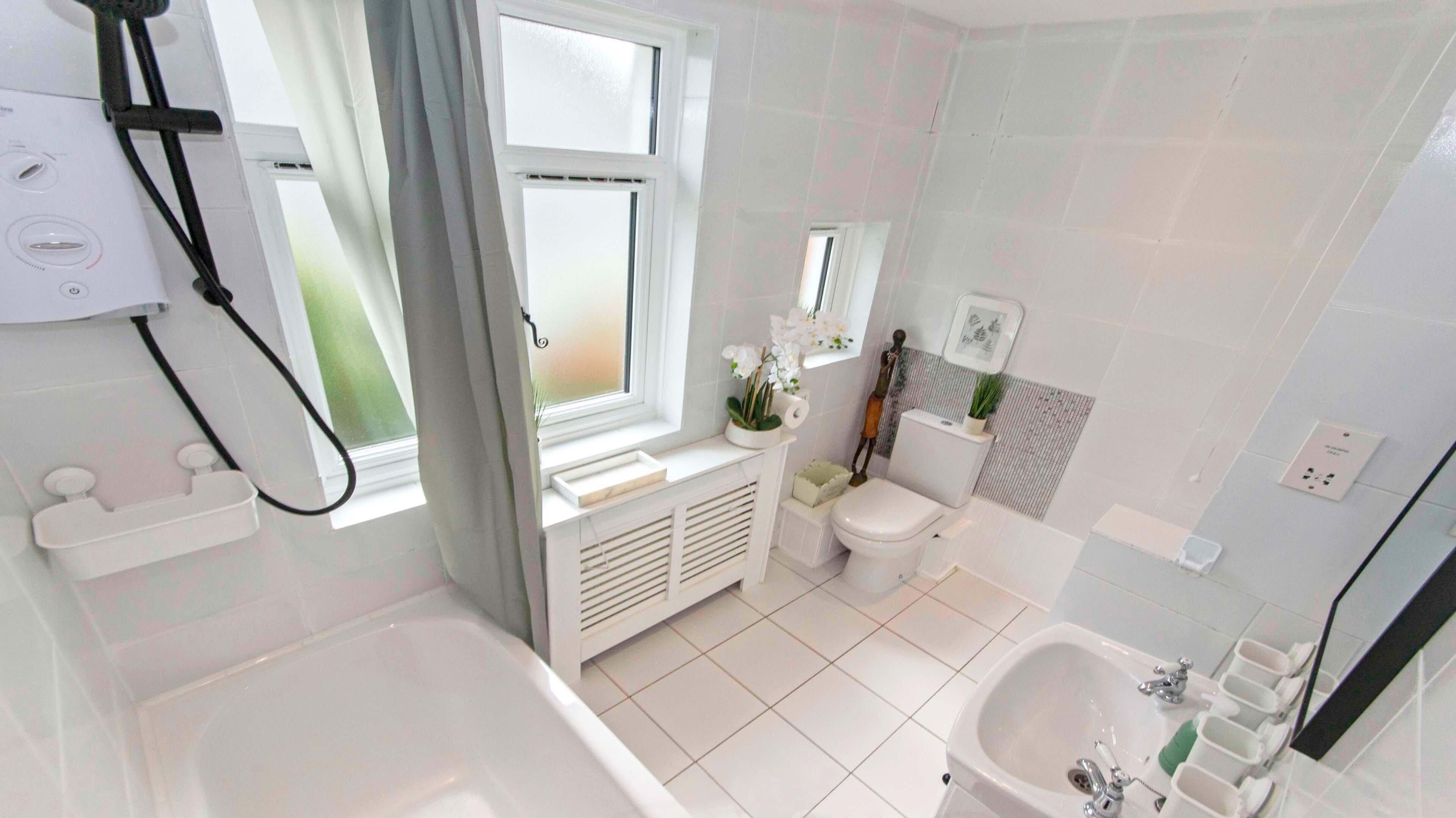 Un baño con bañera, inodoro y lavamanos, con accesorios blancos y una ventana con cortinas.